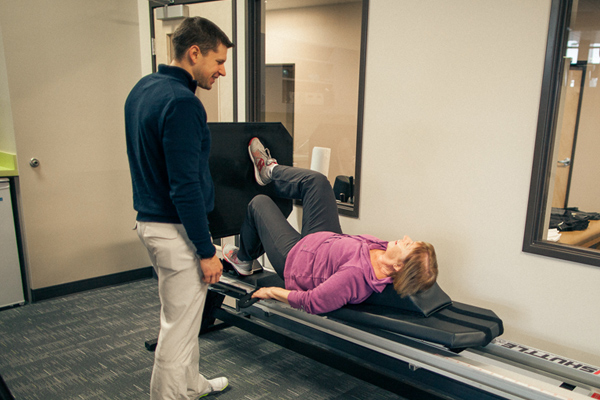 male physical therapist monitors female member performing one-legged leg press