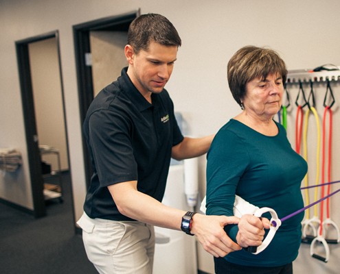 male physical therapist provides assistant to female client with exercise band