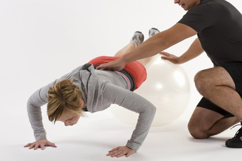 Personal trainer assists client doing a push up with feet on ball