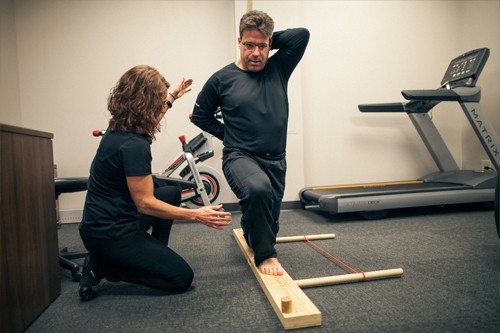 female physical therapist assists male perform lunge exercise