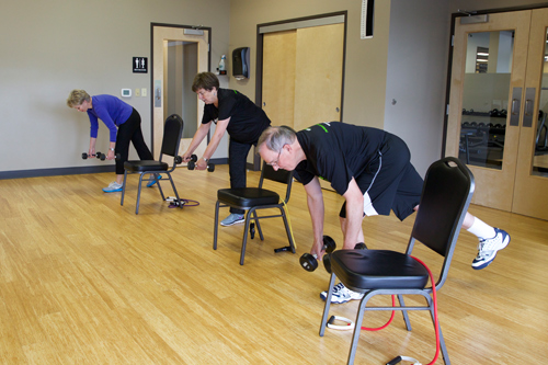 members of senior fit class perform one legged exercise with dumbbells