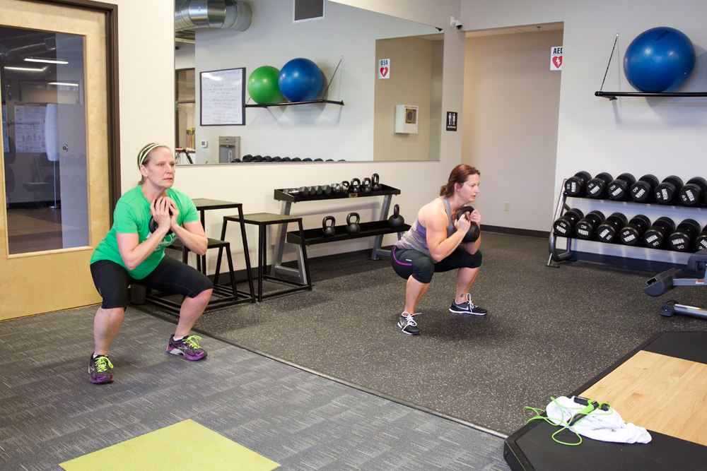 two females performing squat exercise with kettleball