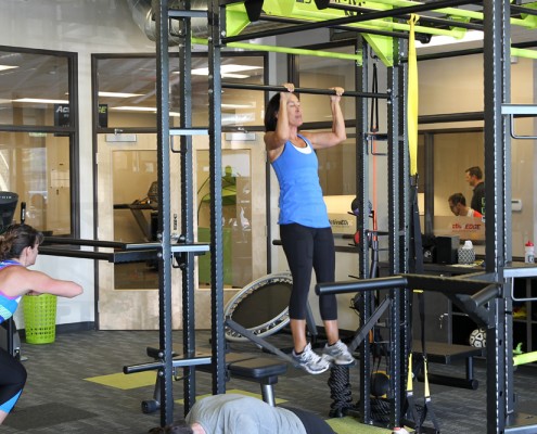 female doing pull-up on bar in health club