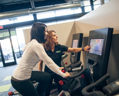 female physical therapist instructs female client on stationary bicycle