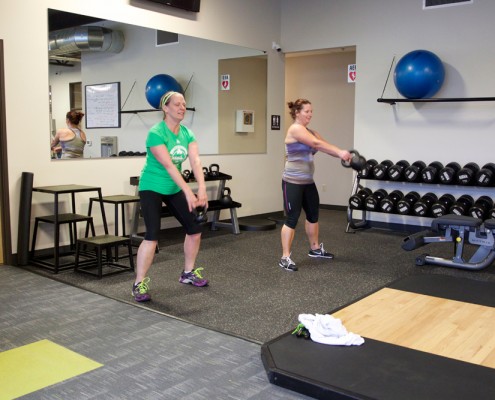 two female members lifting kettleballs in gym room