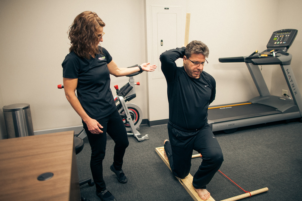 female physical therapist assists male perform lunge exercise