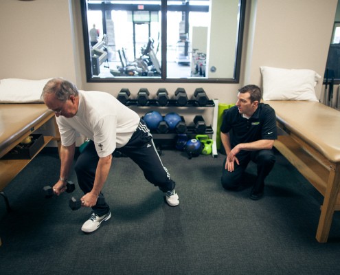 physical therapist monitors male client perform weighted lunge exercise