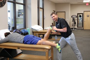 male physical therapist provides stretching assistant to member lying facedown on table
