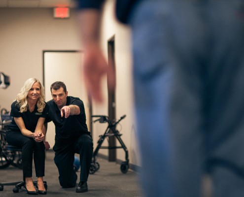 female physical therapist seated, male physical therapist kneeling beside female